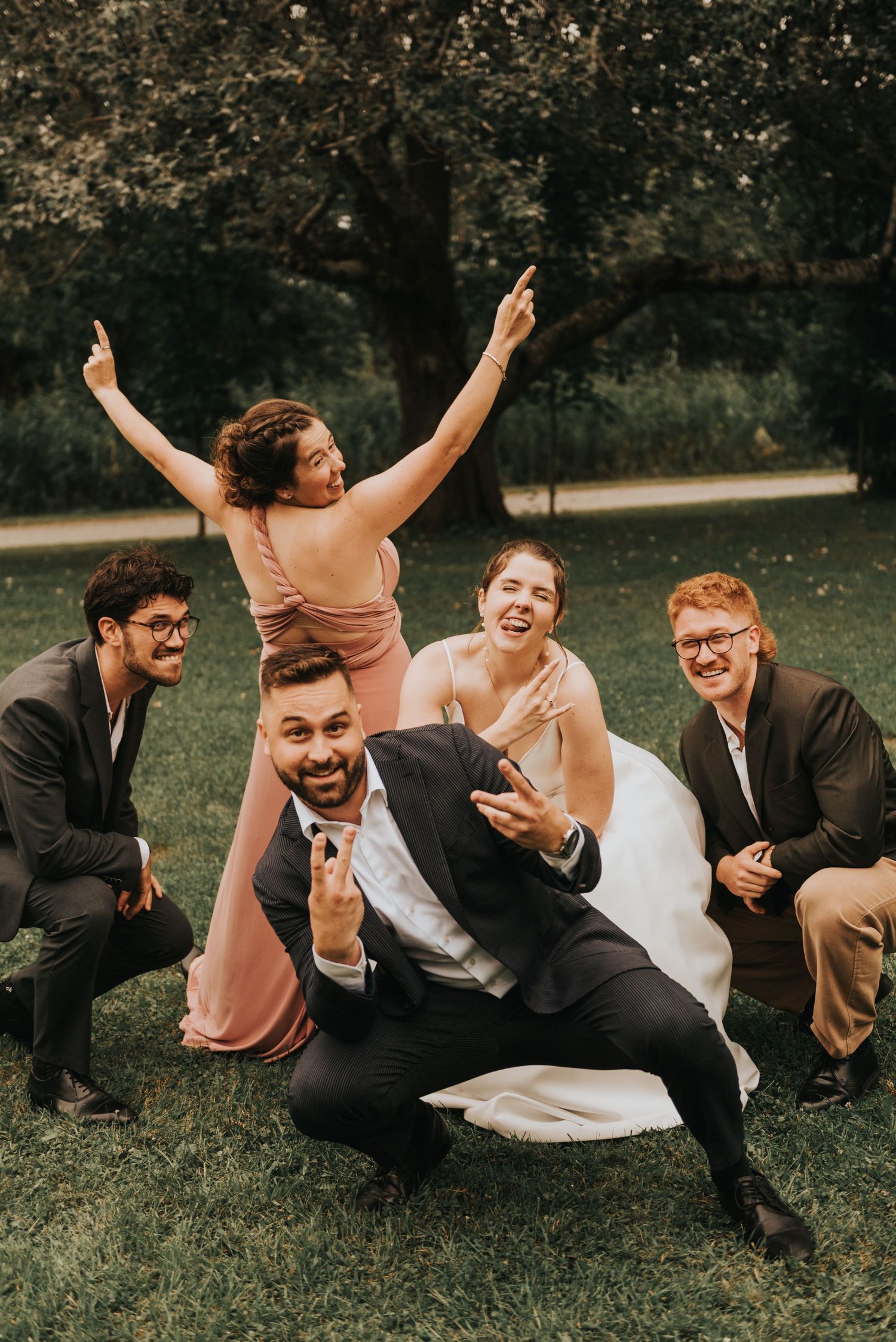 Wedding party having fun and laughing together while posing for candid photos on grass in outdoor setting.
