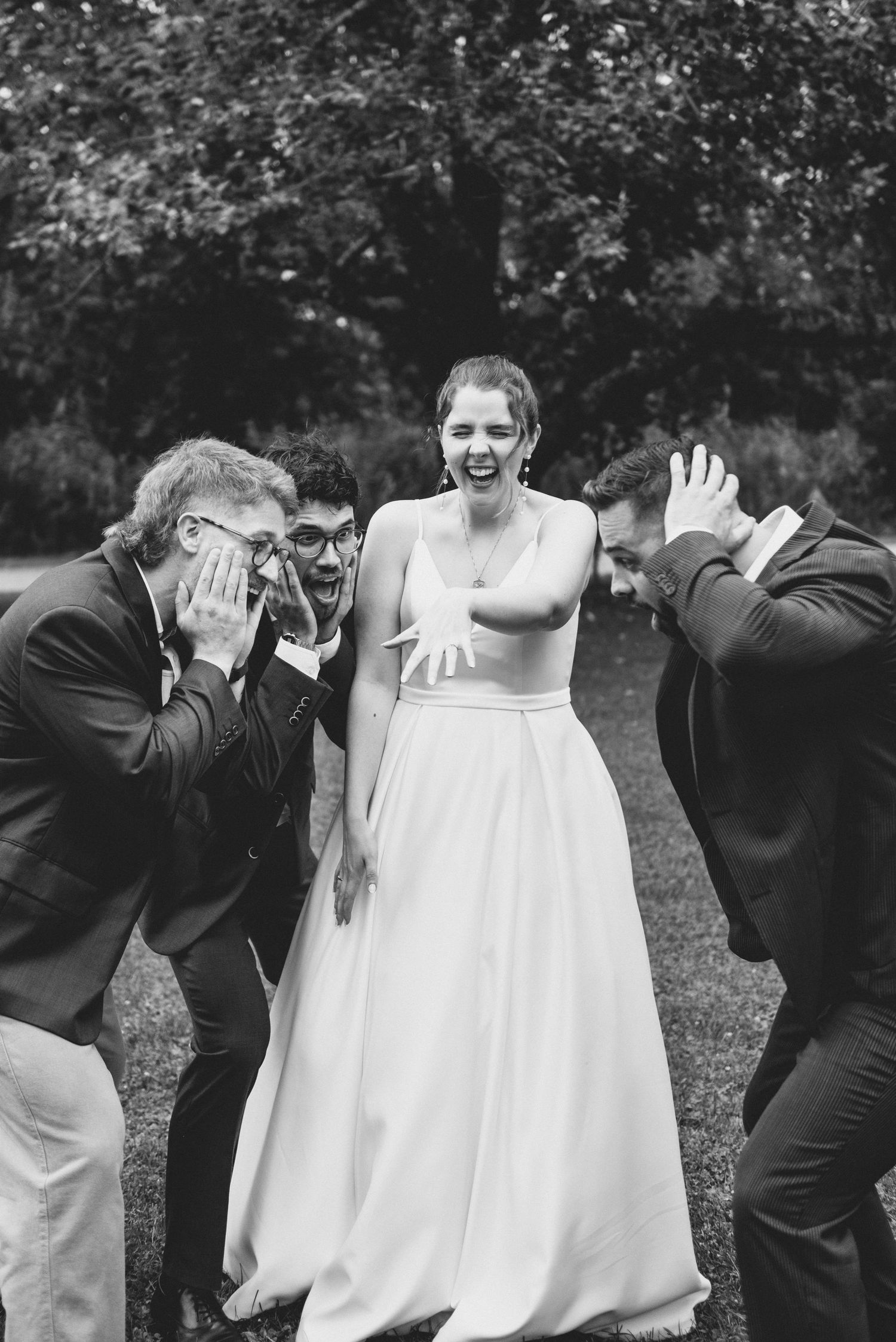 Playful black and white wedding photo showing joyful reactions in an outdoor garden setting.