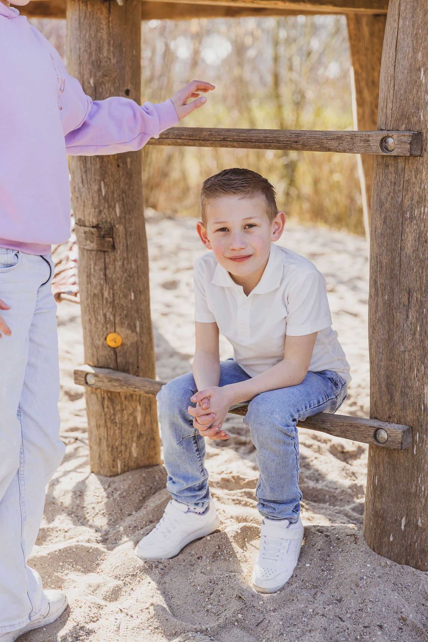 Young person sitting on wooden playground equipment on a sunny day. Ongewdongen op de foto.
