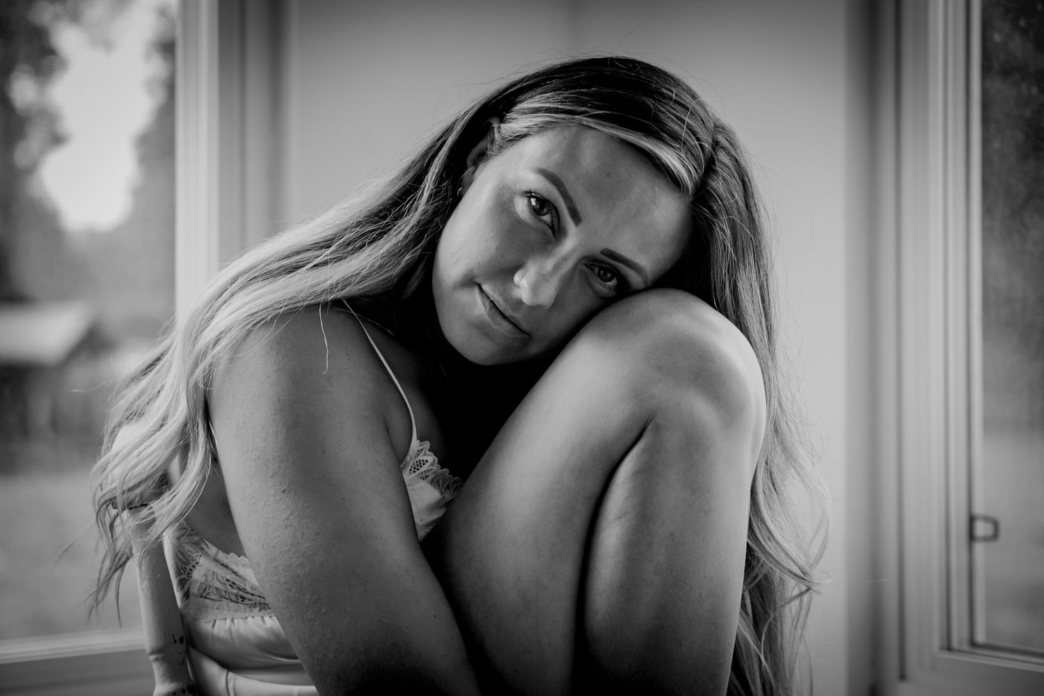 Artistic black and white portrait showing a woman in contemplative pose near window.
