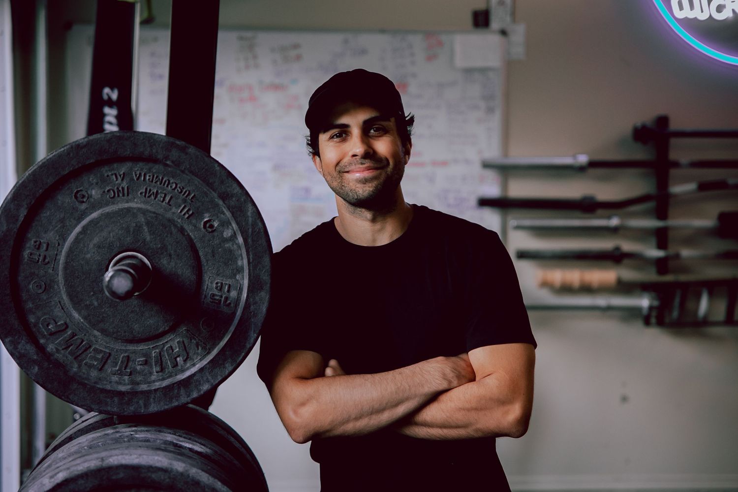 Fitness trainer in gym standing next to weight plates with arms crossed.