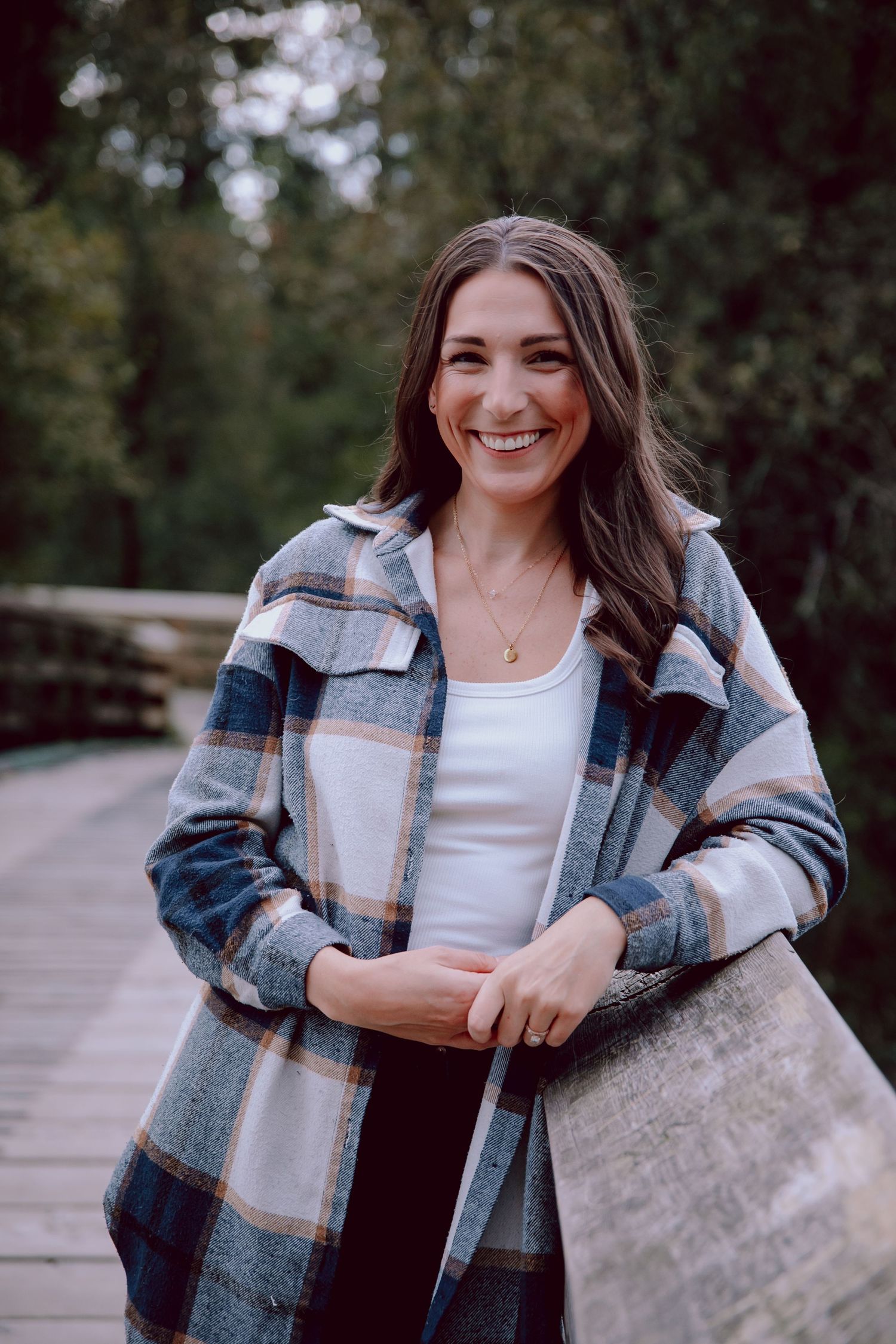 Portrait of woman in plaid flannel jacket smiling on wooden bridge walkway.