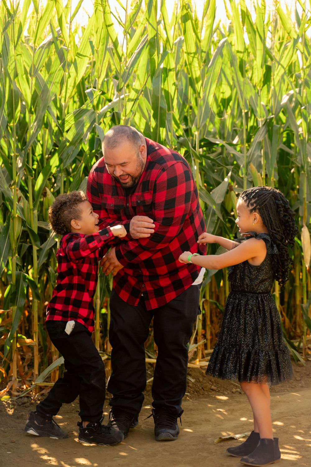 Playful interaction between two people wearing matching red plaid shirts in front of corn stalks.
