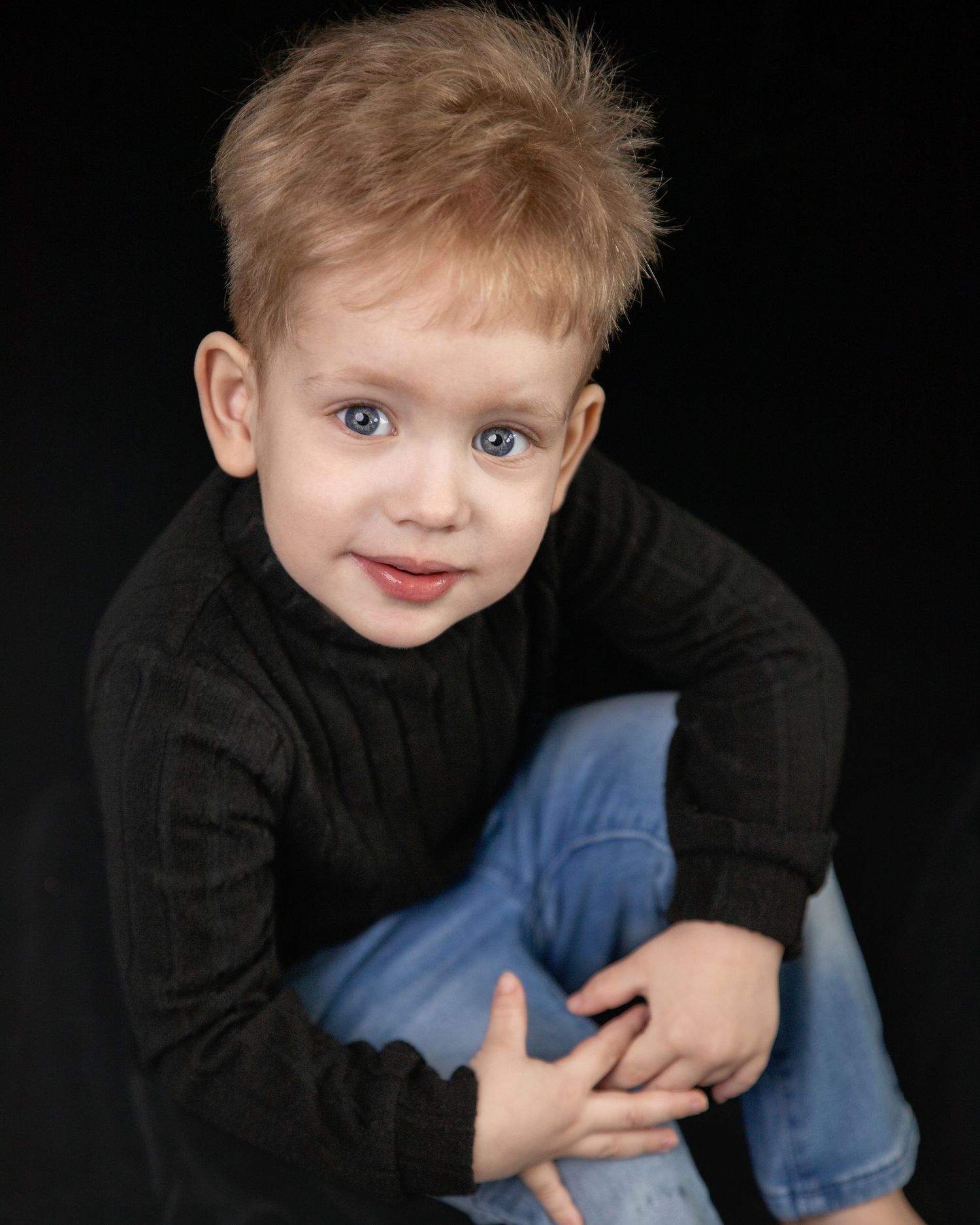 A series of black and white studio portraits showing a child in a black sweater and jeans against a dark background.