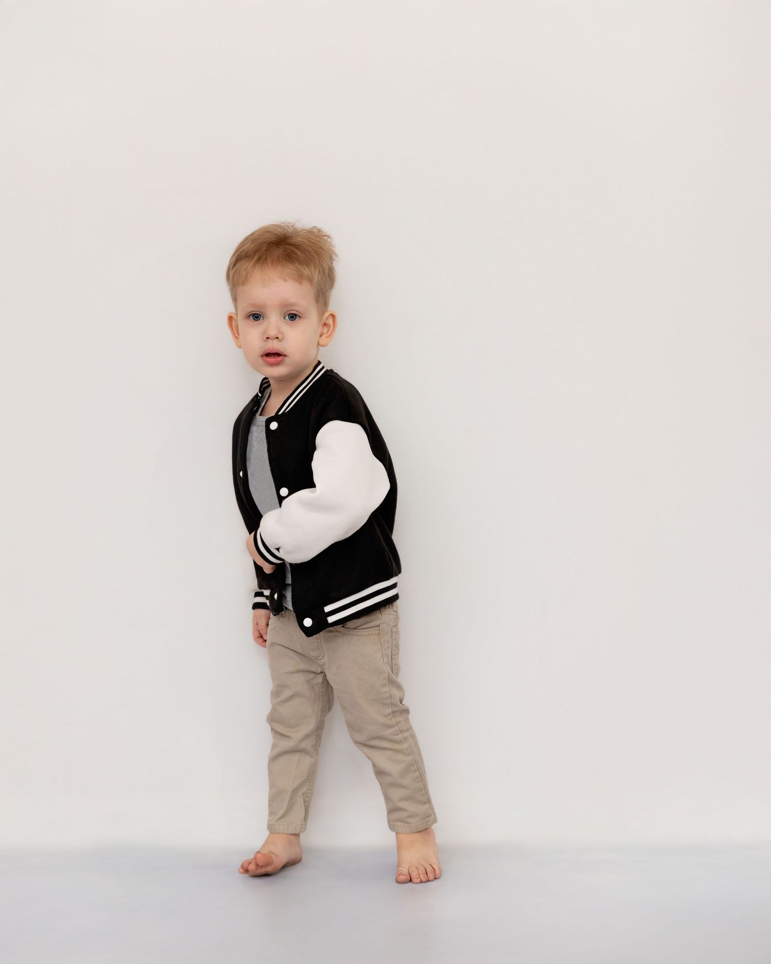 Small child in black and white striped vest and khaki pants poses against white backdrop.