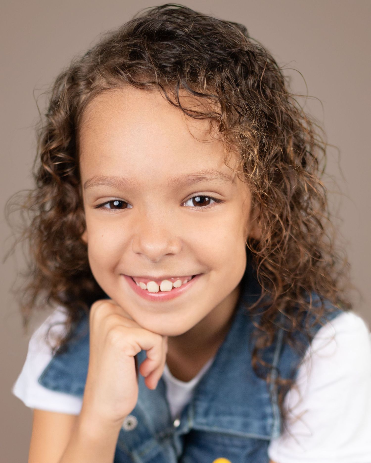 A child with curly hair wearing a denim shirt shows a range of playful expressions in a photo collage.