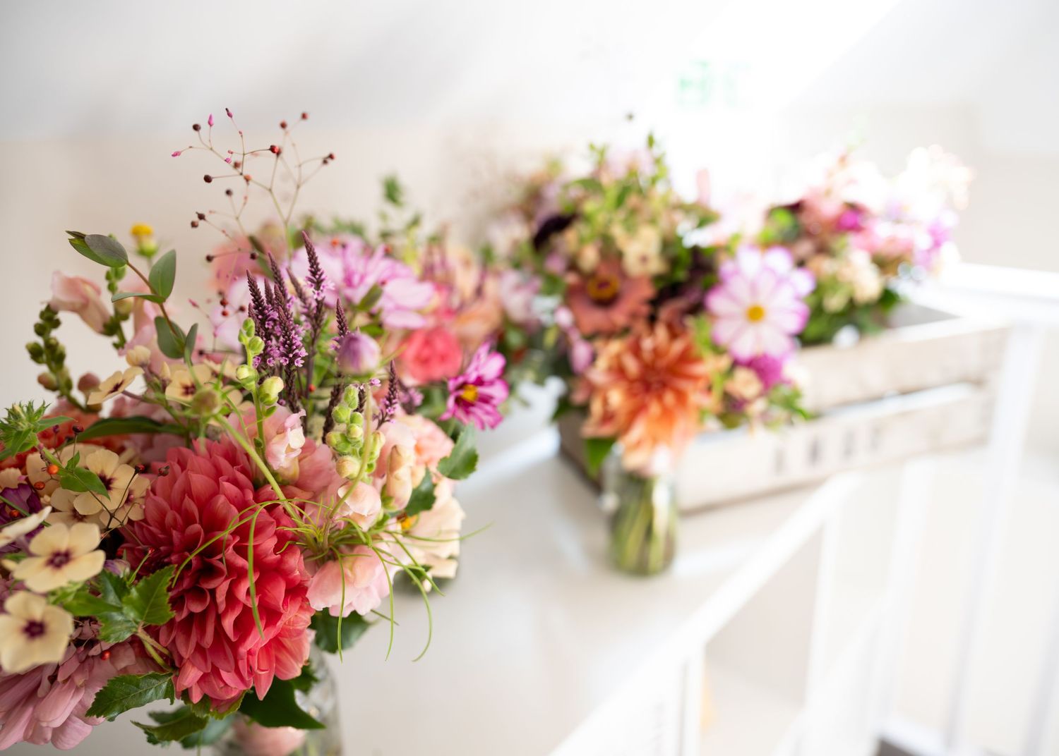 Vibrant pink, coral, and purple fresh flower bouquets arranged on a white surface in natural light.