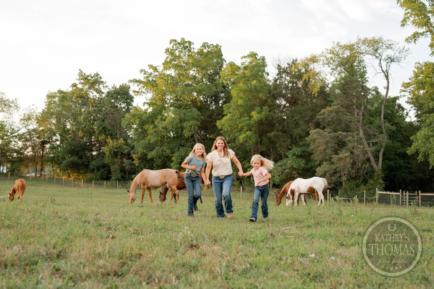 Family enjoying time together in a spacious field with horses grazing nearby at sunset.