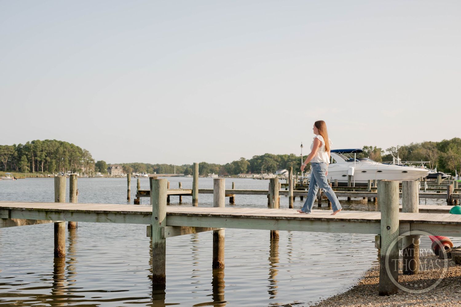 Person walking on a wooden dock at sunset with boats and water in the background.