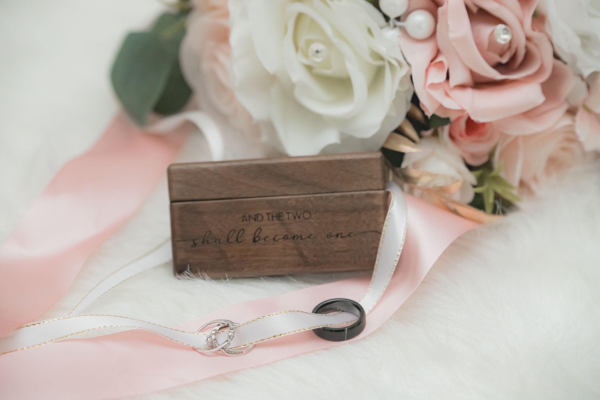 Delicate pink and white roses arranged with rustic wooden decor elements on soft pink fabric.