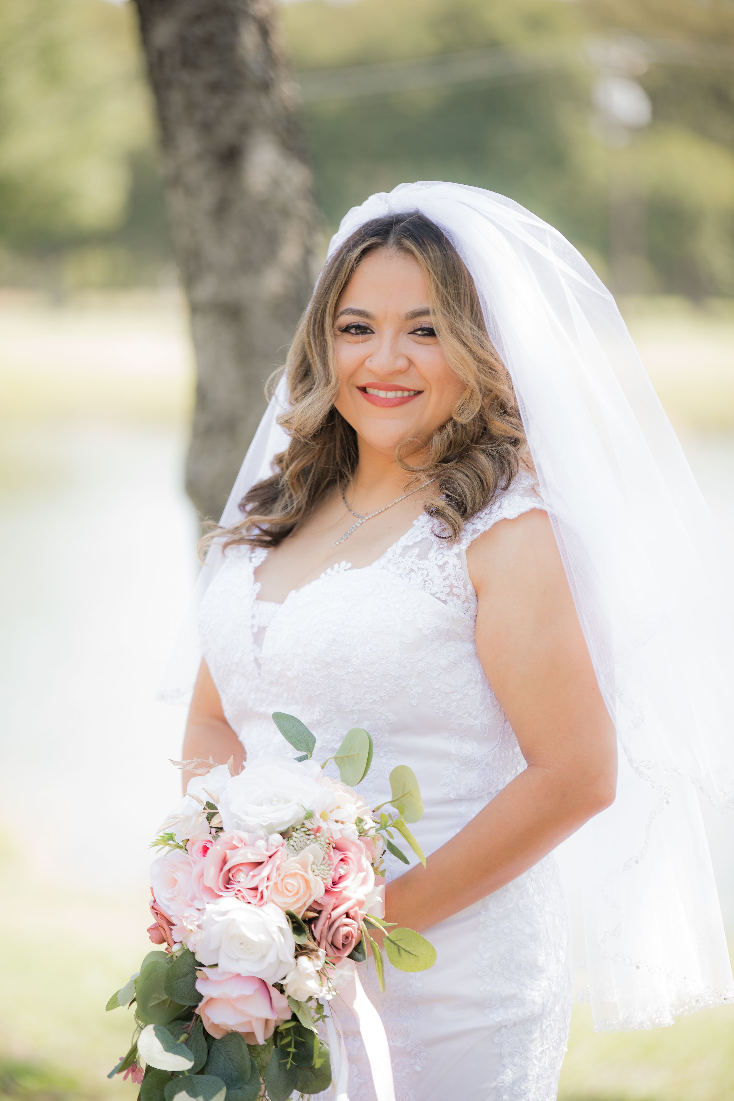 Elegant white lace wedding dress with flowing veil captured in outdoor garden setting.