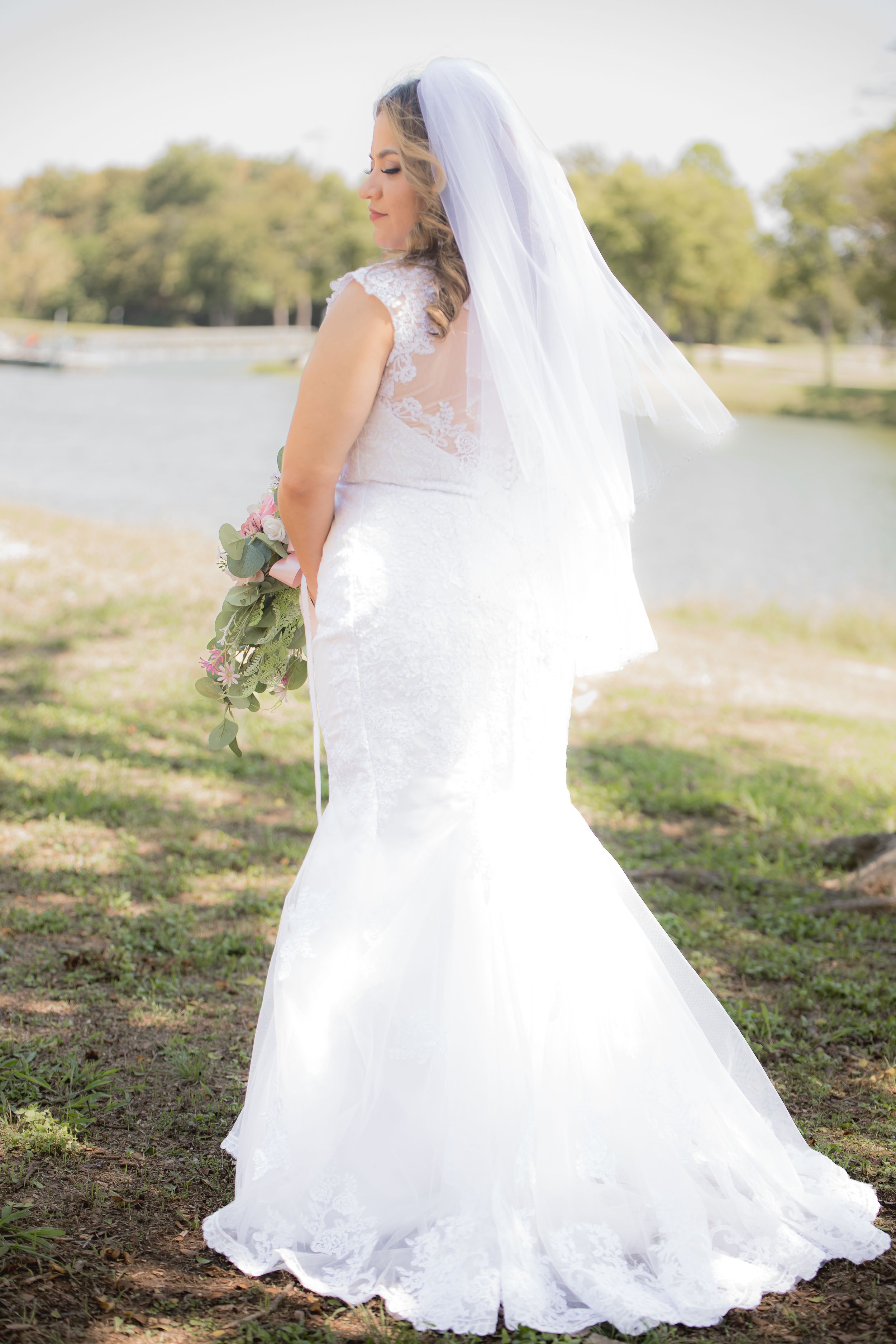 Flowing white lace wedding gown with long train photographed against natural lakeside backdrop.