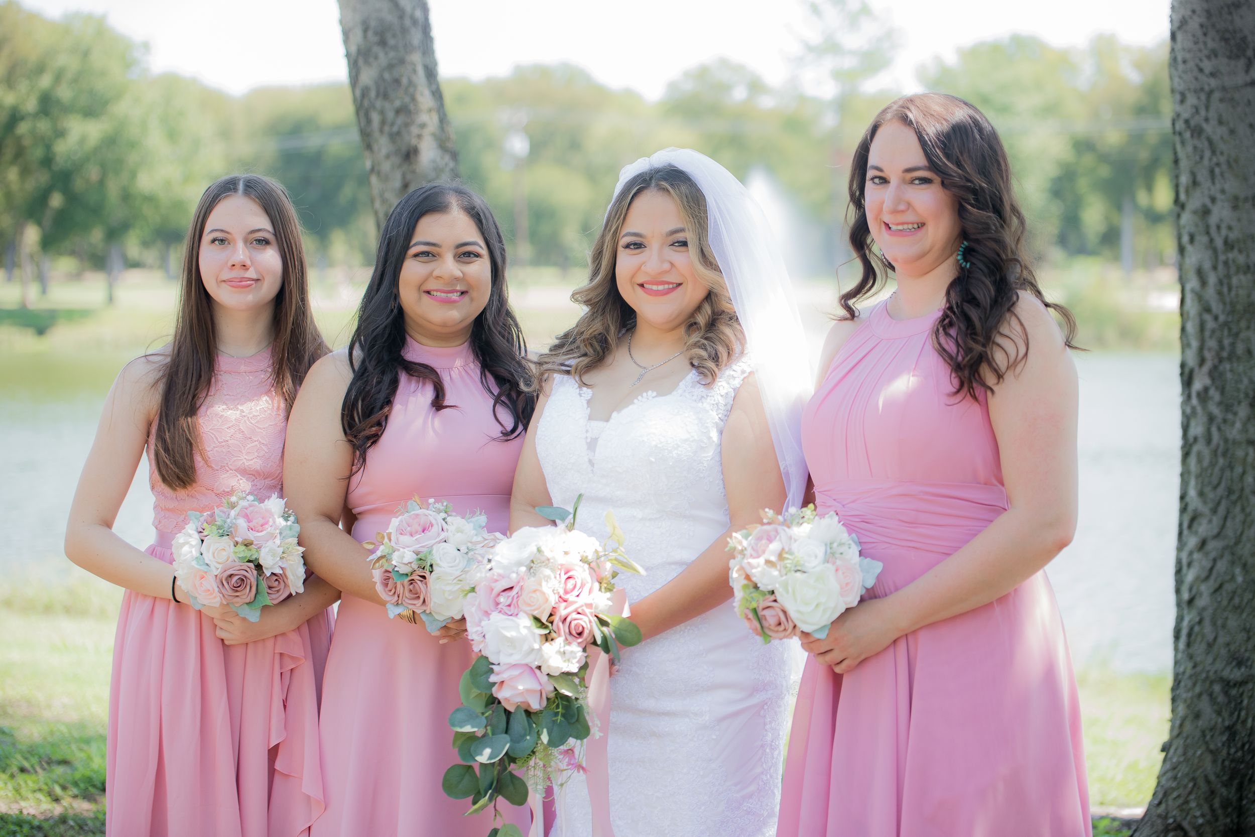 Bridal party in pink dresses posing together outdoors with floral bouquets.