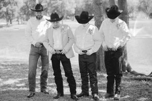 Black and white photo of groomsmen in western attire with cowboy hats lined up outdoors.