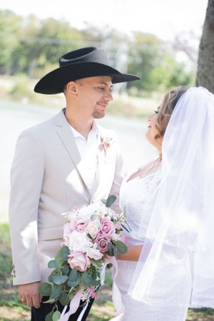Wedding couple in western attire share intimate moments outdoors with pink and white floral bouquet.