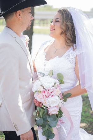 Elegant outdoor wedding scene with white lace dress and pink rose bouquet details.