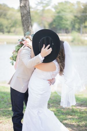 Romantic outdoor wedding photos under trees with white dress and black cowboy hat details.