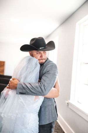 Indoor wedding first look moment with groom in grey suit and black cowboy hat.