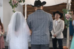 Indoor wedding ceremony moments with grey suit and white dress details.