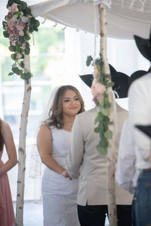 A romantic wedding scene with white birch poles decorated with floral arrangements and soft draping fabric.