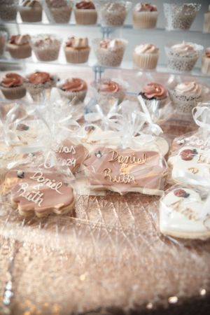 Wedding dessert table with decorated cookies and cupcakes on sparkling display.