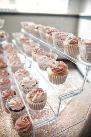 Elegant pink frosted cupcakes displayed on clear acrylic stands with lace wrappers.