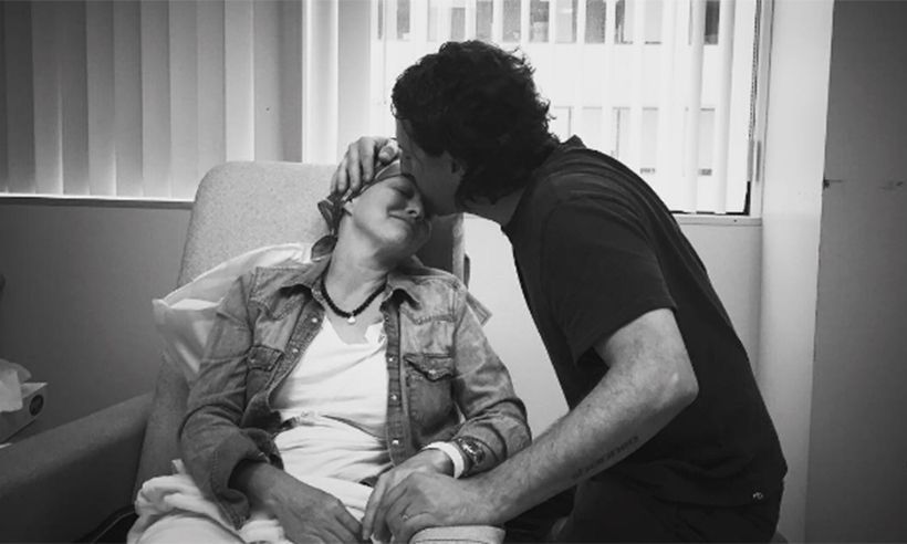A tender black and white photograph shows an intimate moment between two people on a sofa near a window.