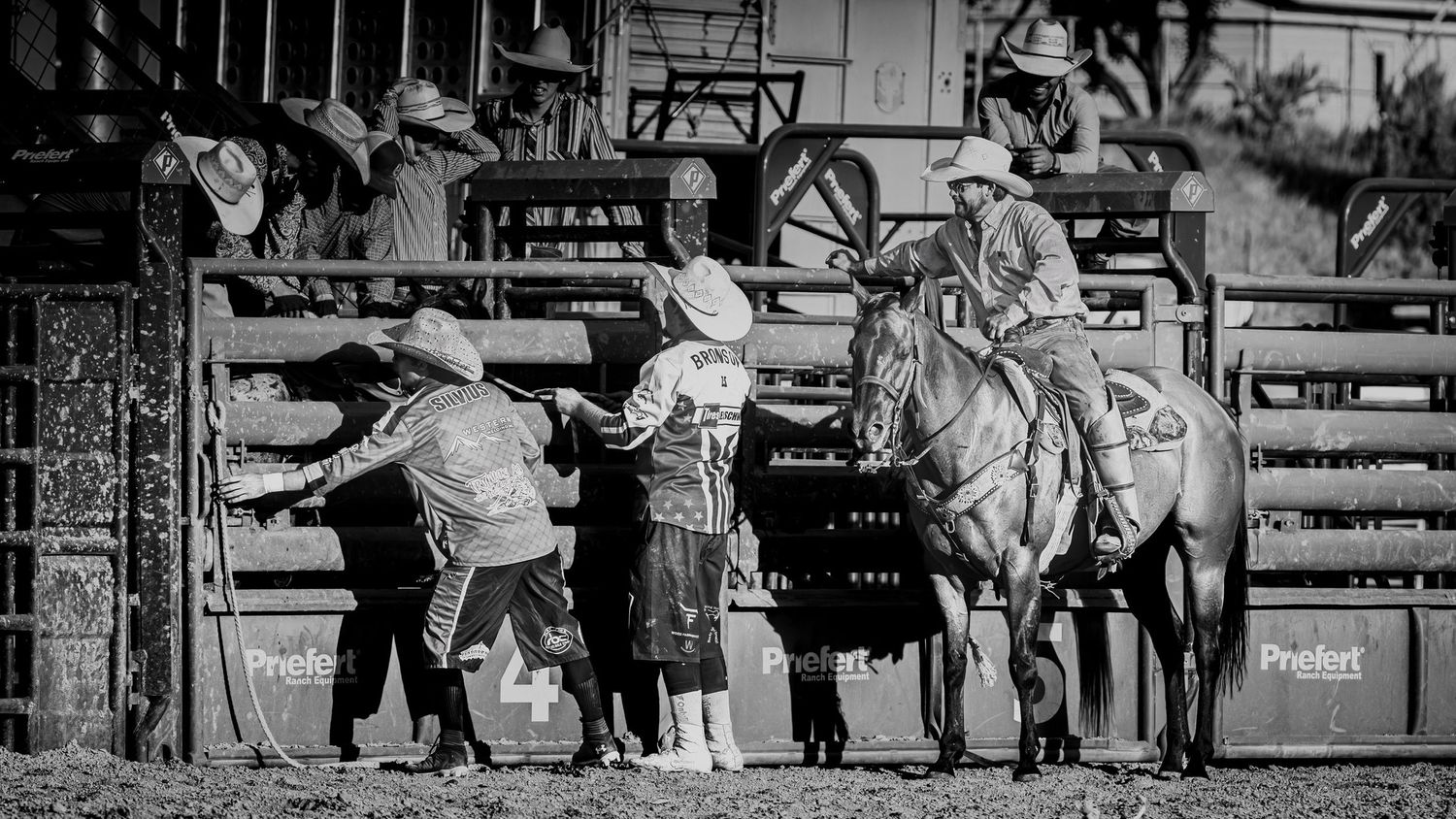 Vintage black and white rodeo scene with cowboys and horses gathered at the arena gates.