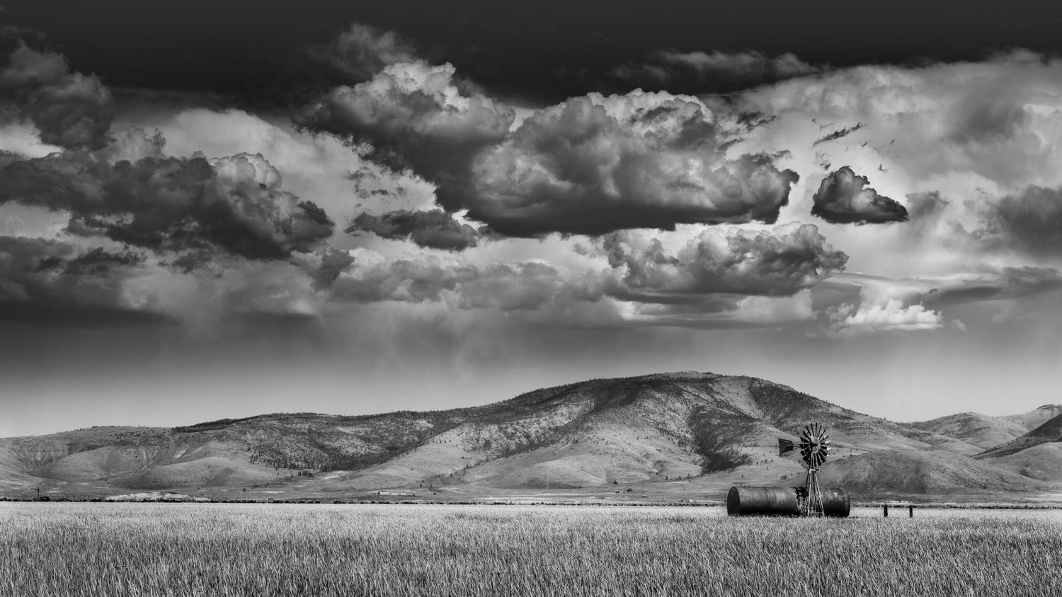 Black and white landscape of rolling hills with dramatic storm clouds and a distant hay baler in a wheat field.