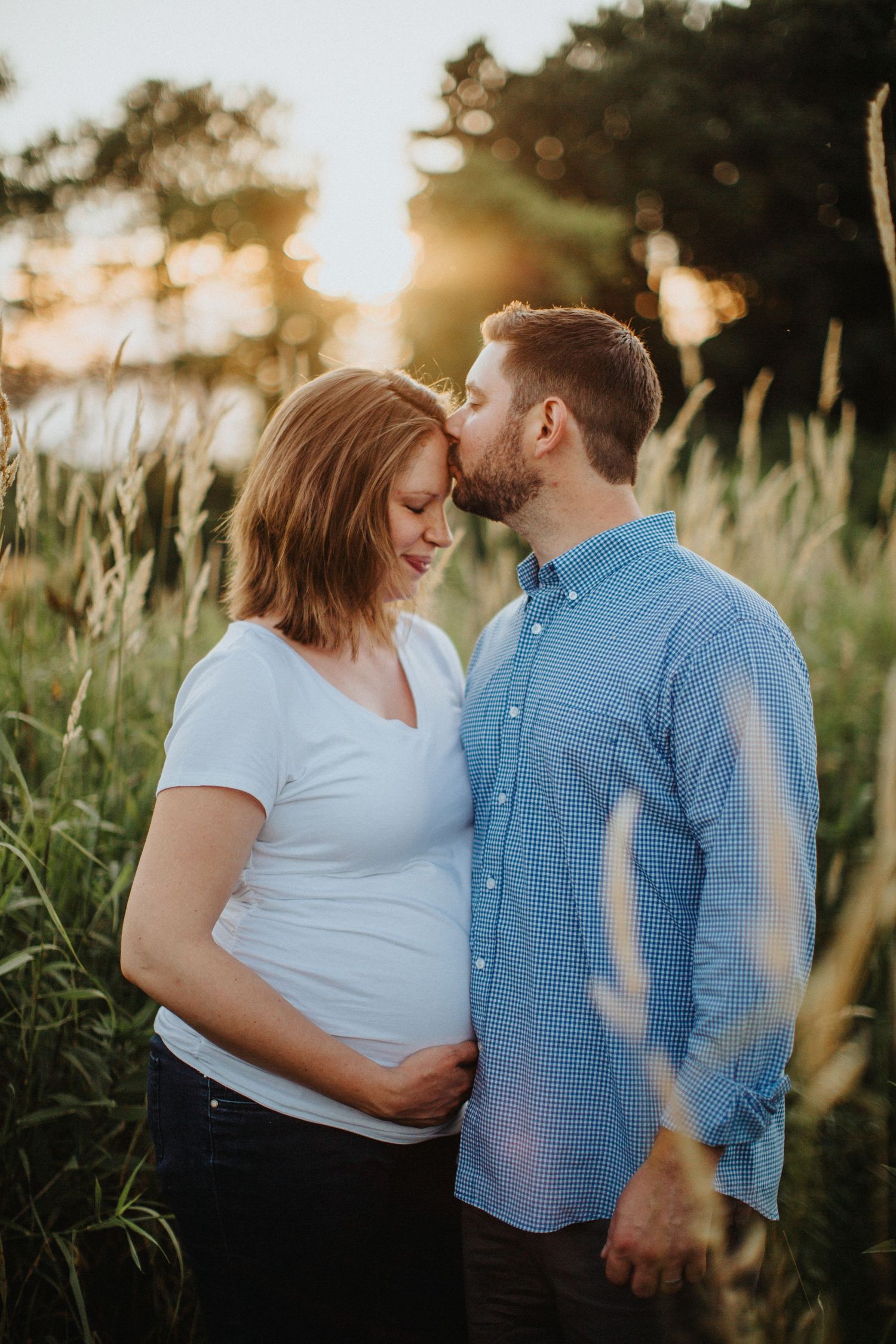 A couple shares an intimate moment in a sunlit field of tall grass during golden hour.