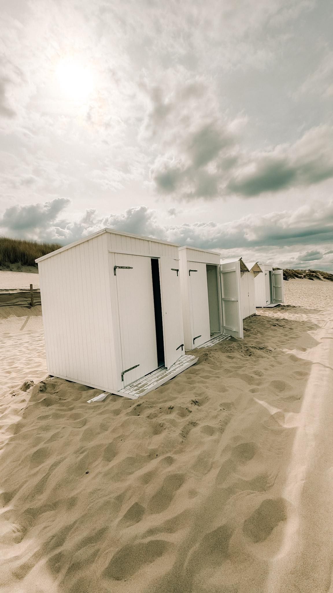 White beach changing cabins on sandy shore with dramatic cloudy sky at coastal beach location.
