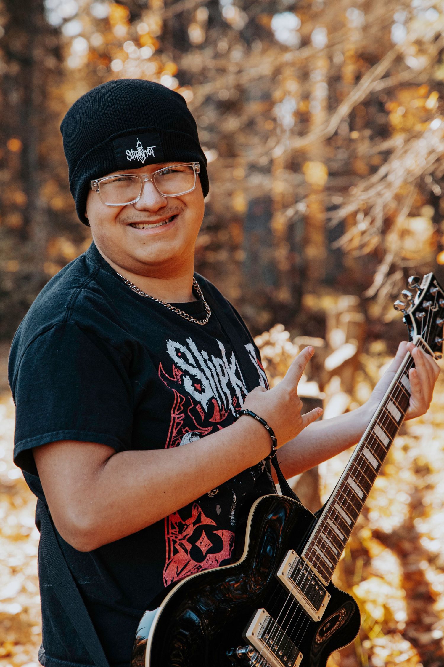Someone stands in front of a blue pickup truck with headlights on in a wooded setting during dusk or dawn.