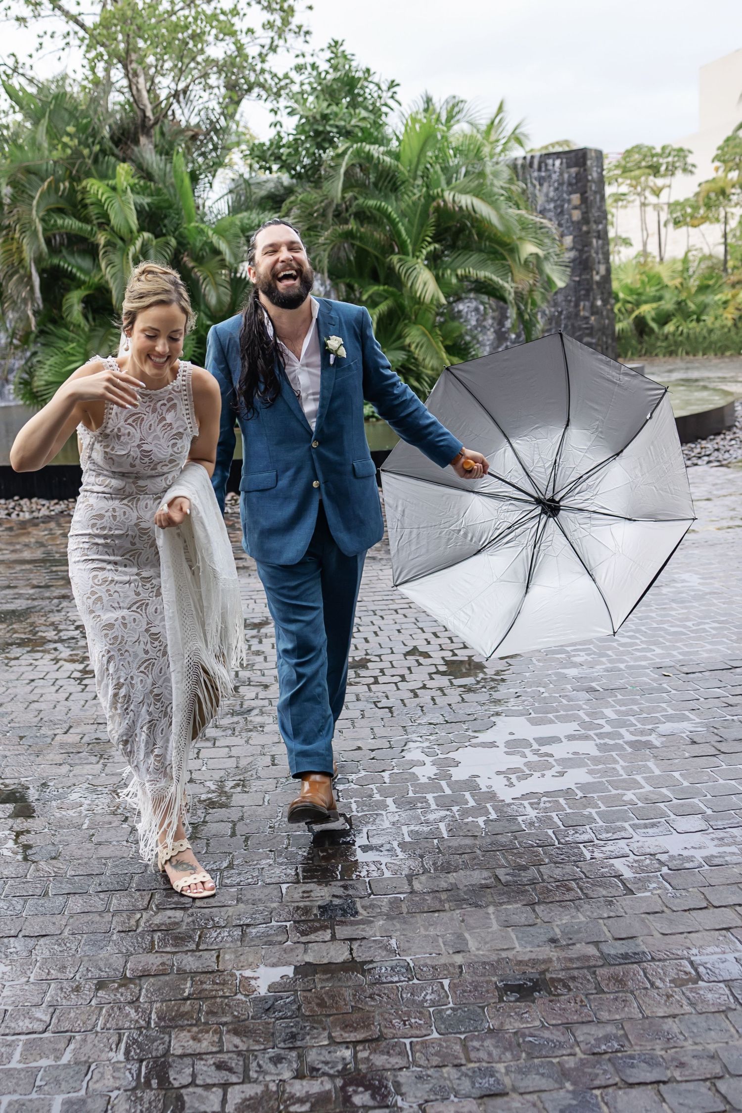 A romantic wedding couple embraces outdoors with lush greenery in the background while sharing an intimate moment.