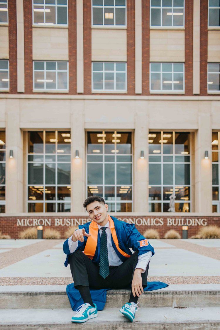 A student in a blue jacket and tie sits on steps in front of the Micron Business Economics Building.