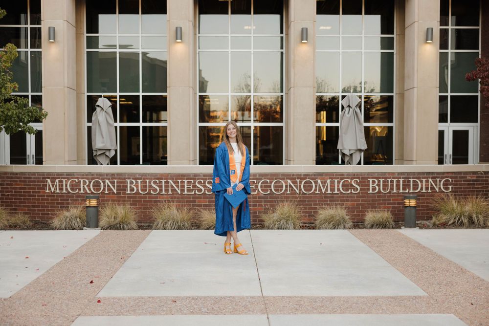 Blue graduation gown against illuminated Micron Business & Economics building exterior with glass windows.