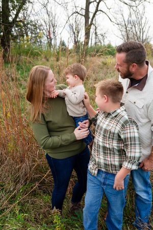 Family of four enjoying an outdoor fall photo session, parents holding a child among autumn grasses with their Marion family photographer.