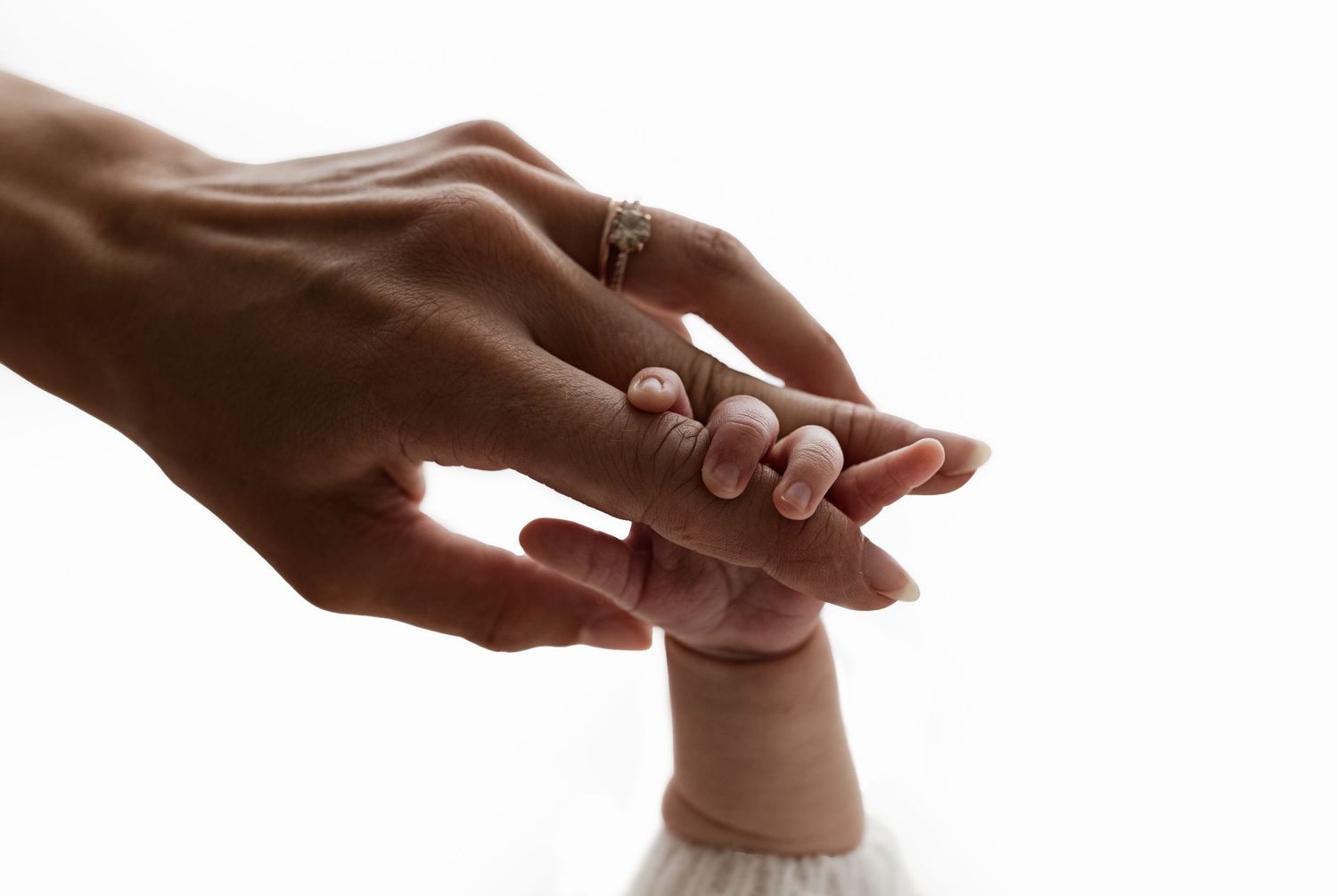 Backlit detail image of a newborn's tiny fingers, clutching her mom's hands, as captured by Charlottesville baby and family photographer.
