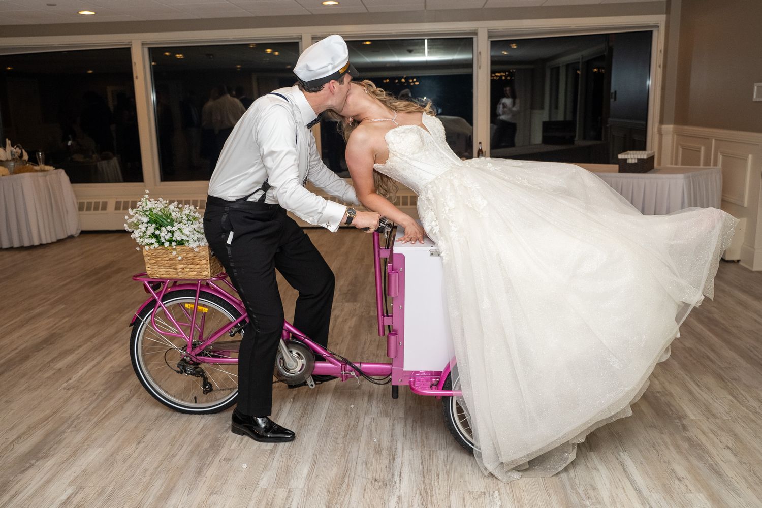 Bride and groom kissing over a pink tandem bicycle at their wedding reception.