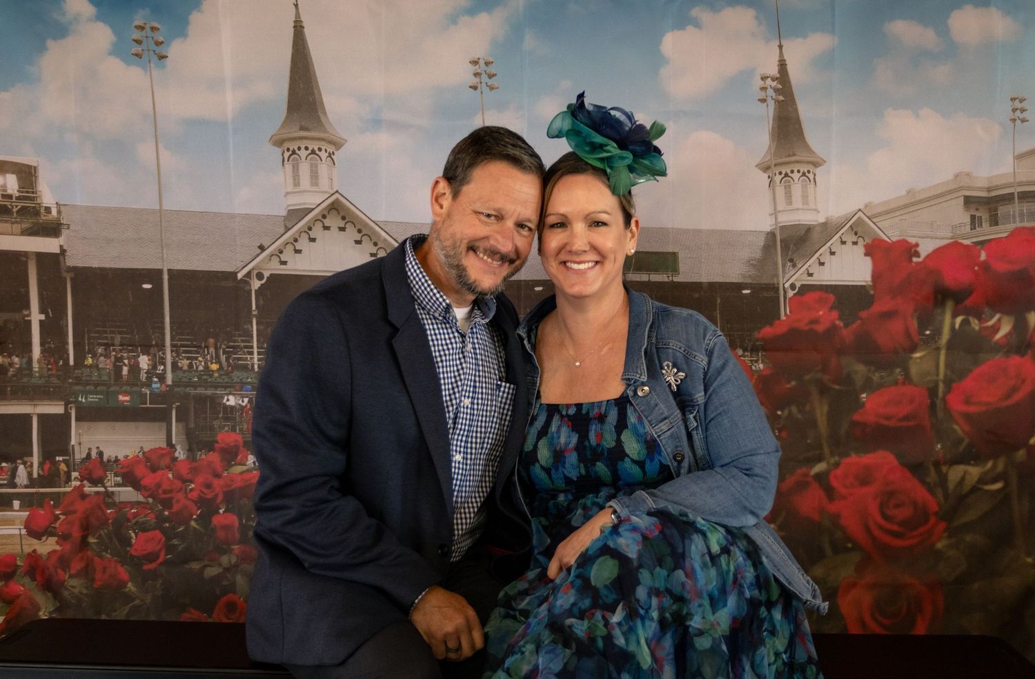 Couple posing together at Kentucky Derby, woman wearing decorative fascinator hat with roses backdrop.