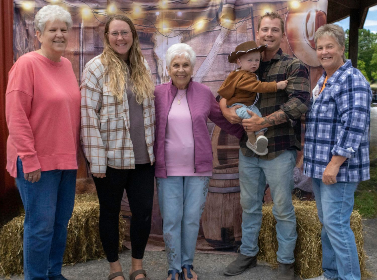 Family group of six posing together at a fall harvest festival with hay bales and rustic barn backdrop.