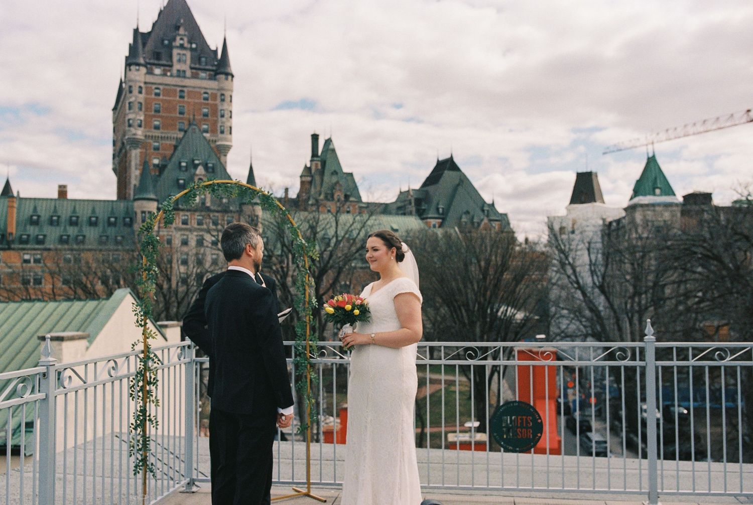 Bride and groom share a romantic kiss in elegant white room with arched window, bride in off-shoulder gown with veil.