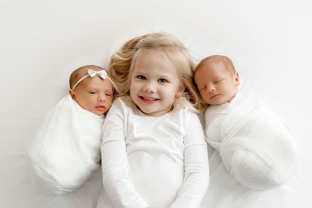 Smiling toddler girl poses with newborn twin babies by Temecula newborn twins photographer.