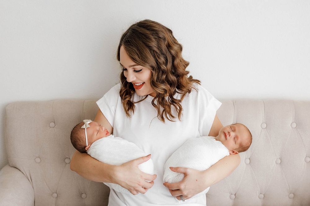 Smiling mother holding two swaddled newborn twins in a bright studio setting by Temecula newborn twins photographer.