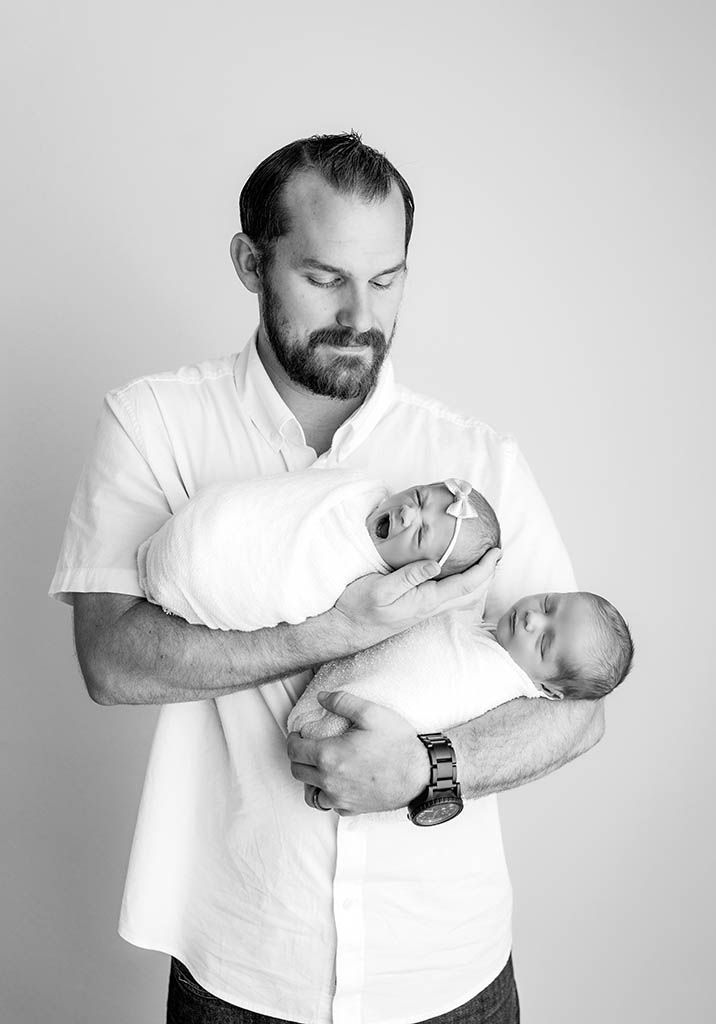 Black and white photo of a bearded father tenderly holding his swaddled newborn baby while looking down lovingly.