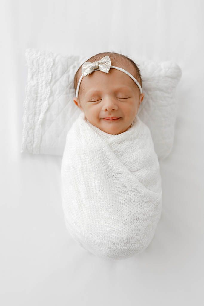Peaceful newborn baby girl swaddled in white wrap with bow headband by Temecula newborn twins photographer.