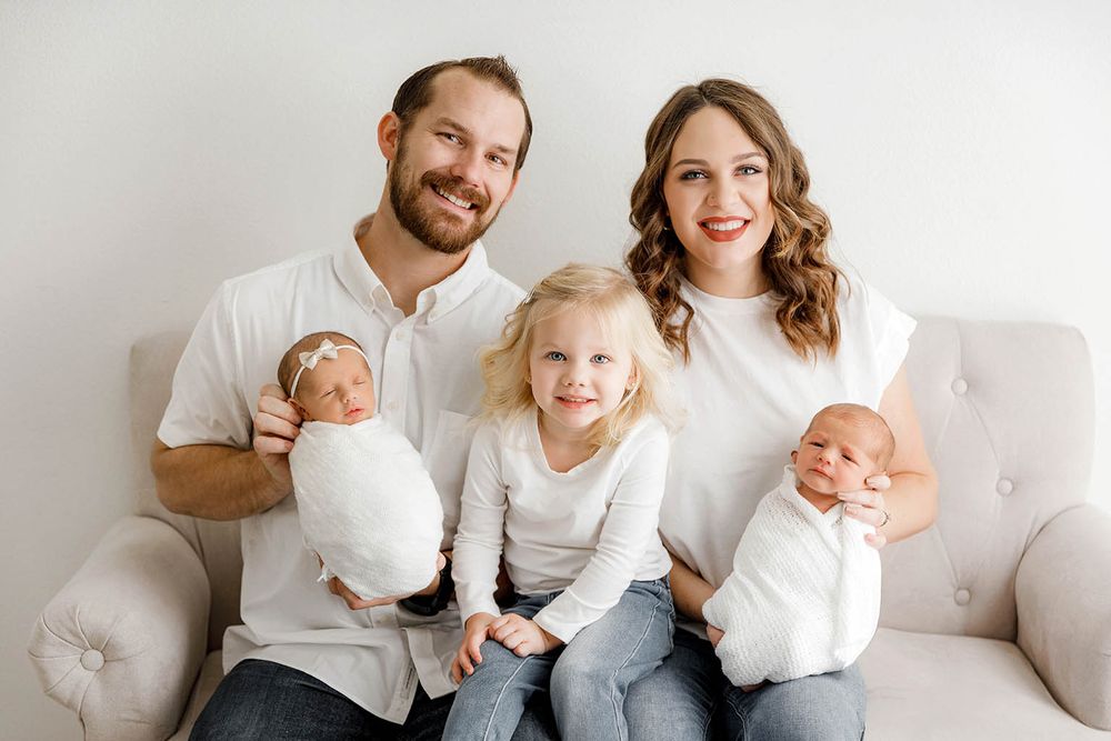 Happy family of five in white tops posing on a sofa by Temecula newborn twins photographer.