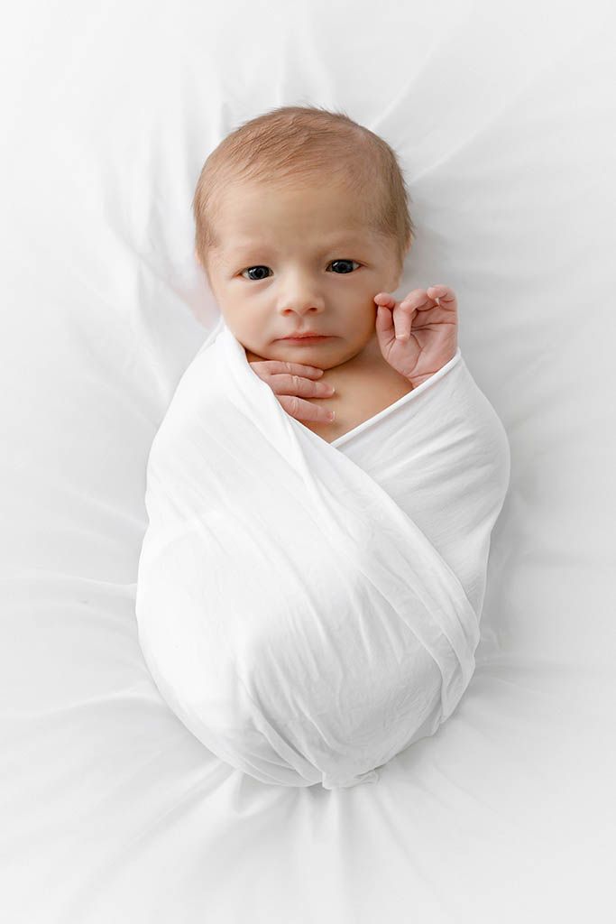 Newborn baby swaddled in white cloth lying on white background by Temecula newborn twins photographer.