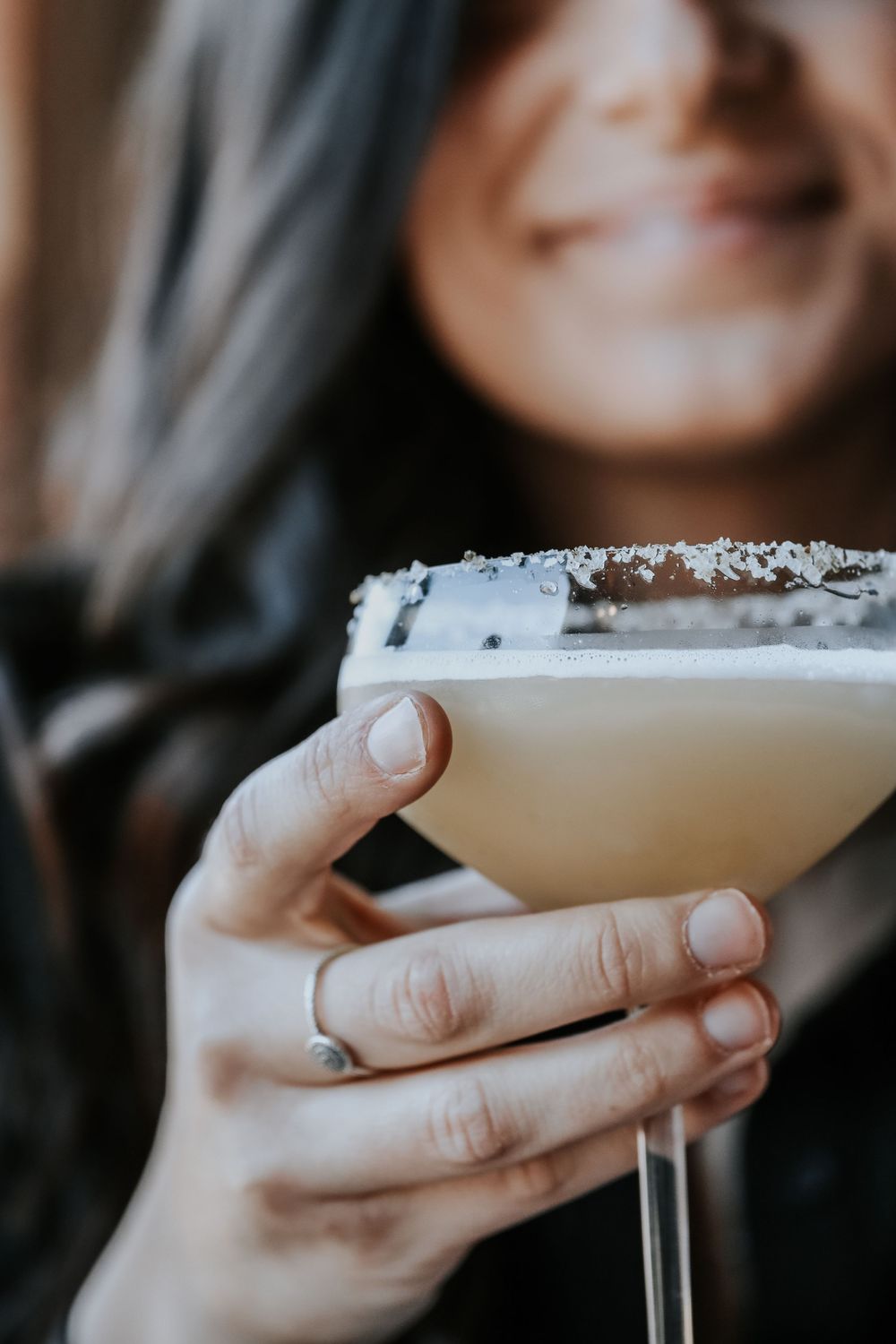 Smiling woman holding a creamy cocktail in a martini glass with a salted rim close-up.