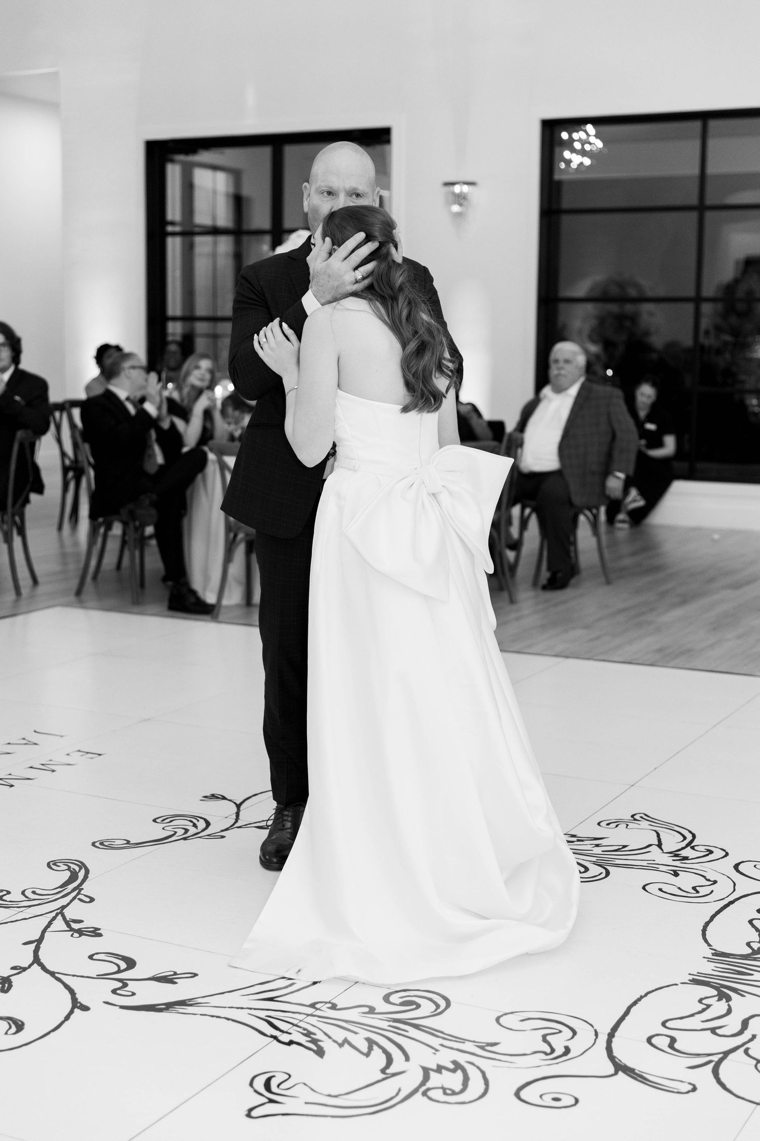 Black and white photo of bride and groom sharing first dance on ornate dance floor at elegant wedding reception.