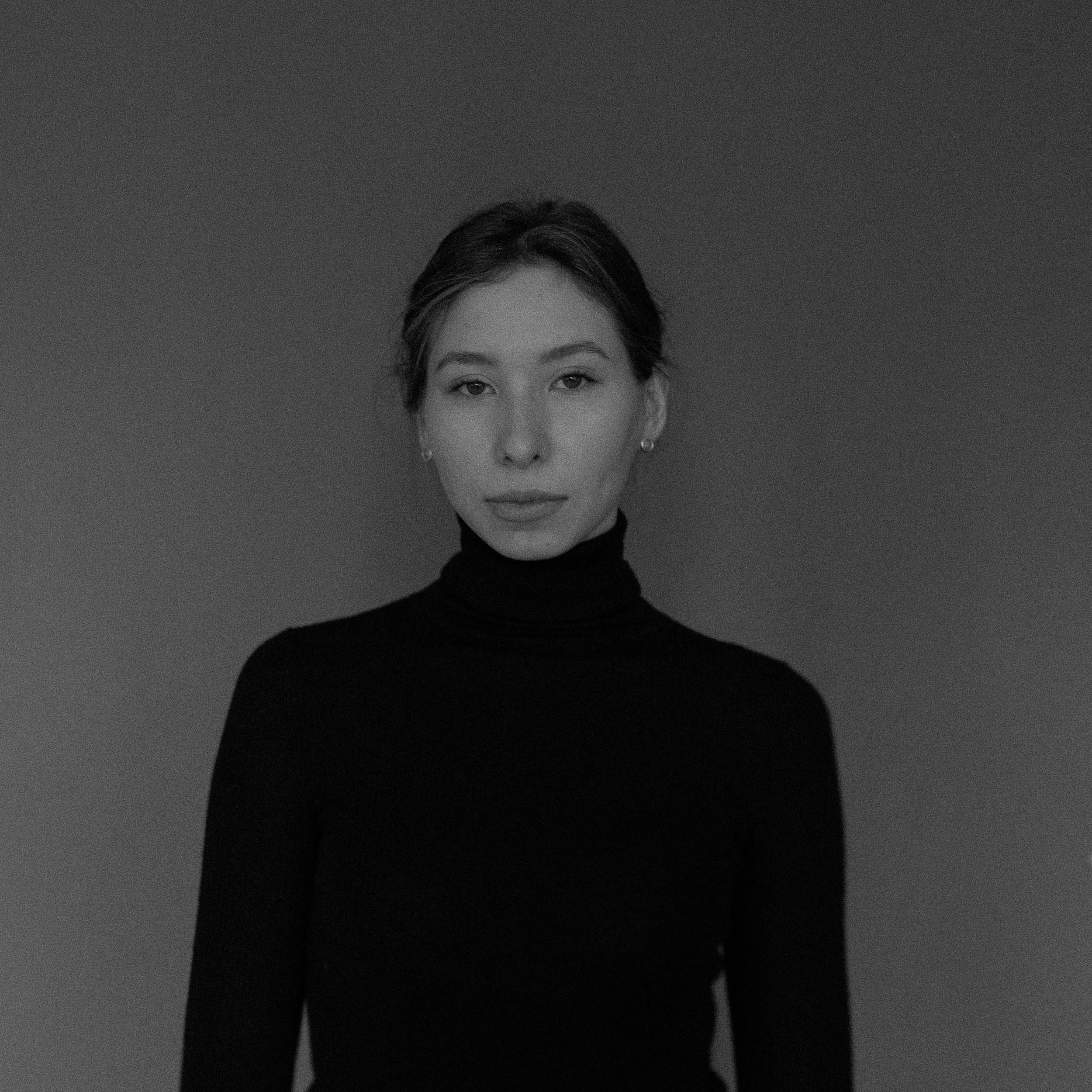 Black and white portrait of a young woman in a black turtleneck sweater against a dark background.
